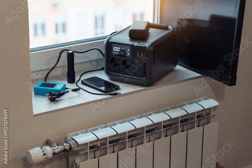 Wallpaper Mural Electricity backup at home in blackout, power outages, heating shutdown, energy crisis. Portable power station, power bank, small solar panel on window sill near home radiator. Torontodigital.ca