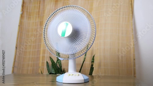 Tabletop oscillating fan providing air circulation, moving from side to side for cooling comfort. Home appliance for hot weather.