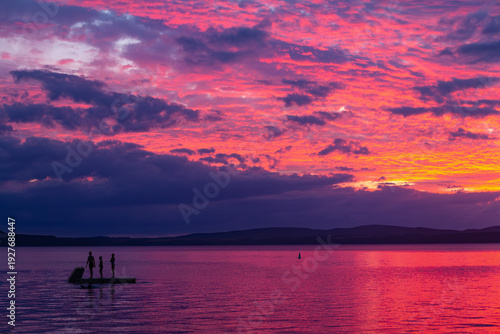 Wallpaper Mural Sunset at Lake Taupō, New Zealand. 3 silhouetted swimmers on swim platform. Whangamatā Bay, Kinloch. Vivid pink, purple sky. Torontodigital.ca