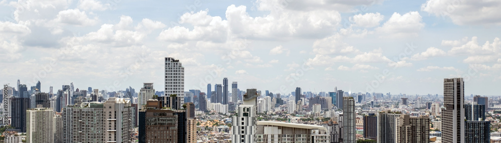 Obraz premium Expansive city skyline with dense high-rise buildings under a bright, cloudy sky, showcasing a modern urban metropolis.