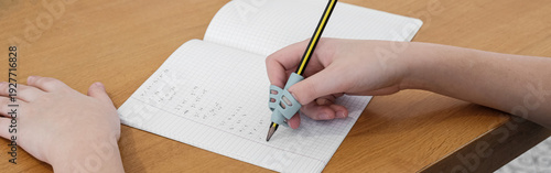Child practicing handwriting with a special finger grip trainer. Close-up of kid's hand holding pencil correctly. Development of fine motor skills and calligraphy.