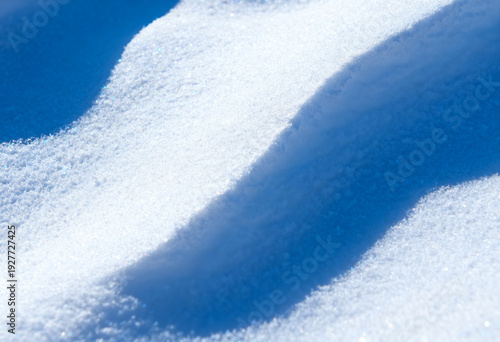 Soft white snow surface texture. Sparkling ice crystals, blue shadow. minimal background, cold seasonal backdrop, frozen landscape macro pattern for holiday design. nature wallpaper