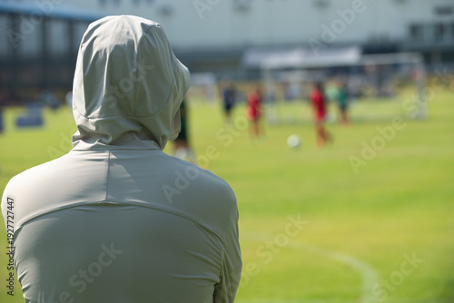Candid back view of a supportive Asian father cheering for their son during a youth soccer match at school.