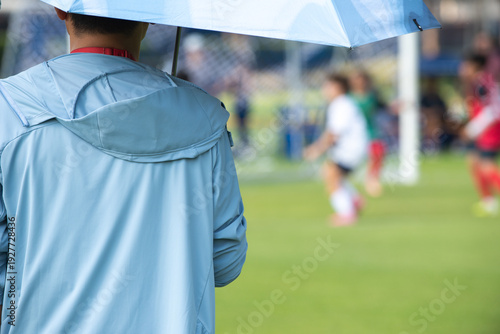 Candid back view of a supportive Asian father cheering for their son during a youth soccer match at school.