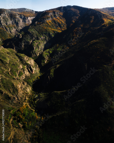 Mountain valley landscape with autumn forest and dramatic hills under blue sky