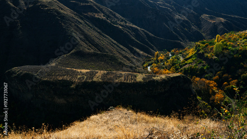Mountain valley landscape with autumn forest and dramatic hills under blue sky