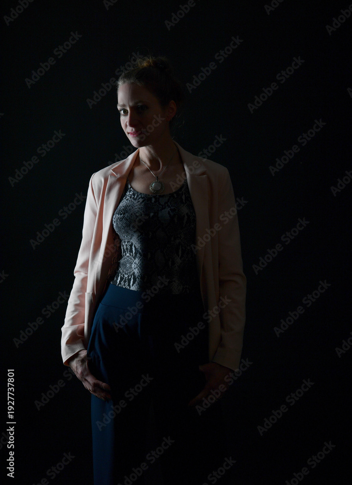 Naklejka premium Low-Key-Portrait eines Models im Mantel vor dunklem Hintergrund. Dramatisches Licht, starke Schatten und roter Lippenstift setzen elegante, ausdrucksstarke Akzente.