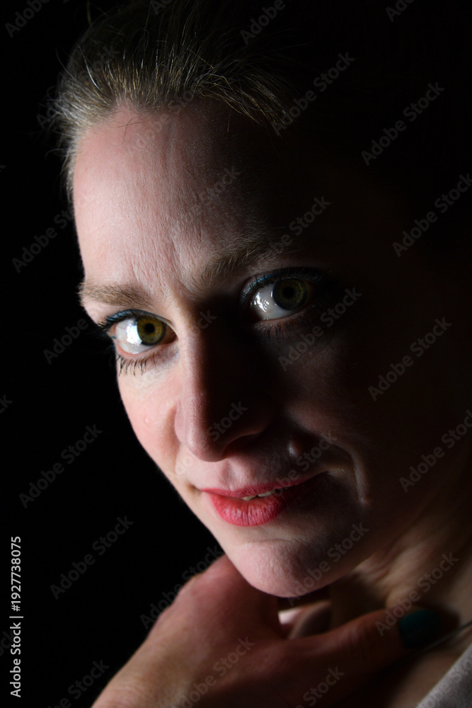 Obraz premium Low-Key-Portrait eines Models im Mantel vor dunklem Hintergrund. Dramatisches Licht, starke Schatten und roter Lippenstift setzen elegante, ausdrucksstarke Akzente.