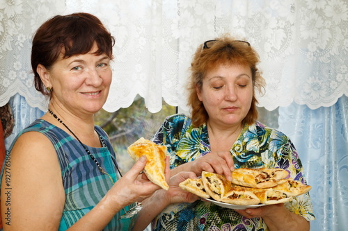 Two cheerful mature sisters eat hot cakes