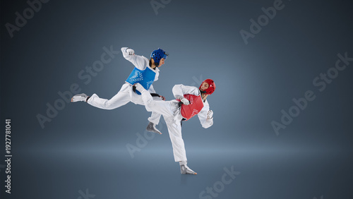 Professional taekwondo fighters in dynamic kick exchange on blue background wearing protective helmets and chest guards. Concept of elite combat sport, competitive sparring and athletic performance.