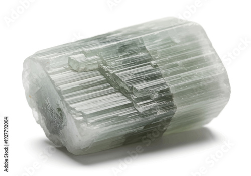 A detailed view of a crystal mineral specimen showcasing its striated structure and facets on a plain surface from a slightly elevated angle