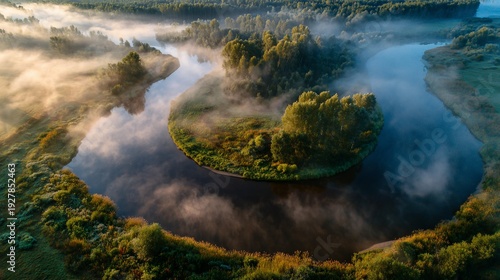 Aerial view of a river bending through a misty landscape, with trees and soft sunlight