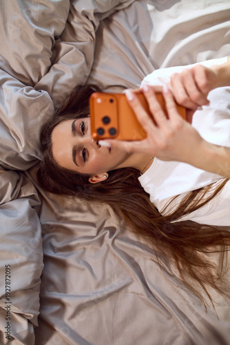 Εκτύπωση καμβά Young woman scrolling on the phone while lying in bed