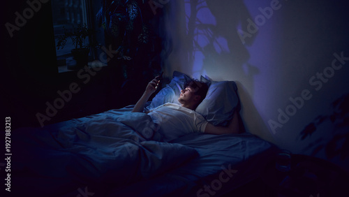 Fotografía Young man lying in bed using smartphone late at night