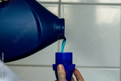 Pouring blue liquid laundry detergent into measuring cap