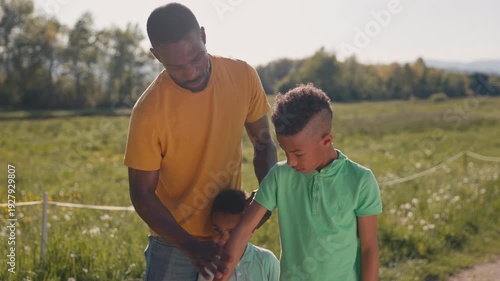 Father paying attention to sun protection for his two sons during summer outdoor activities, applying sunscreen to them, medium shot.