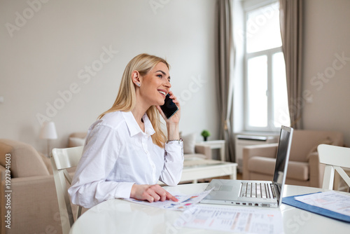 Bild auf Leinwand Professional woman talking on phone while working on laptop at home