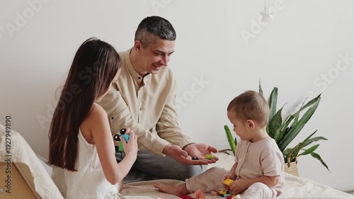 Two children and a man engage in playtime, using colorful toys in a simple indoor area filled with plants and soft light in the afternoon
