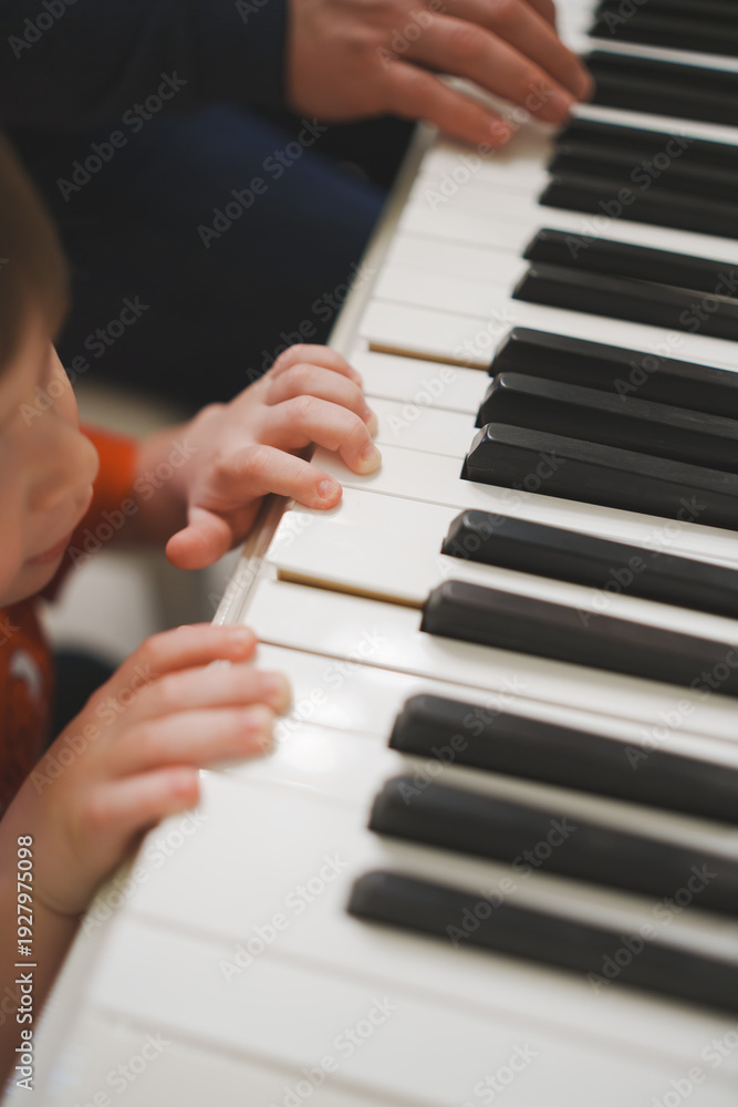 Fototapeta premium Child learns to play piano with adult during music lesson