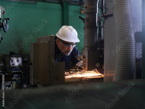 Industrial technician operating grinding machine with sparks in manufacturing factory
