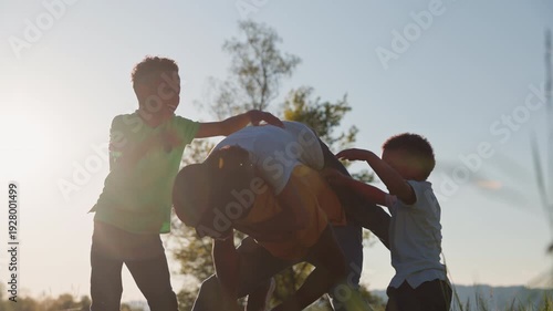 Children playfully wrestling and laughing with their father on a sunny day in a beautiful natural setting, moments of warmth, joy, and family bonding, medium shot.