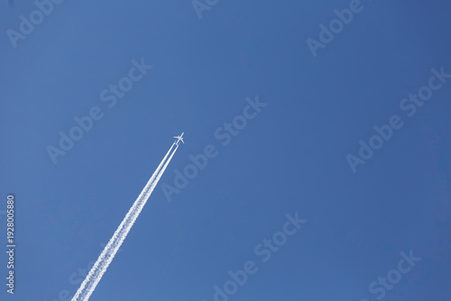 Passenger airplane flying at high altitude, leaving a long white contrail against a clear blue sky. Minimal composition with strong sense of direction