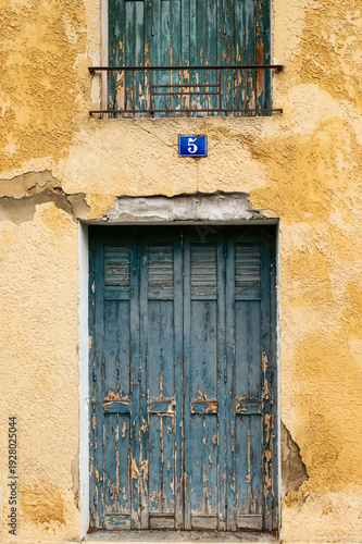 Two old blue shutters on facade of house with door number plaque in L’Isle sur la Sorgue in Provence France 