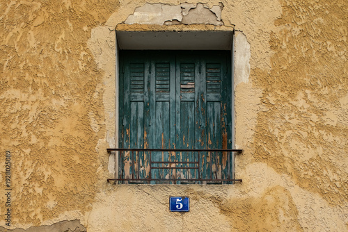 Weather old blue shutter on yellow textured plaster facade in Provence France 