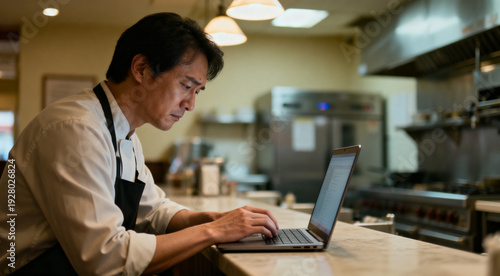 Professional chef and restaurant owner looking stressed while responding to a negative online review on a laptop
