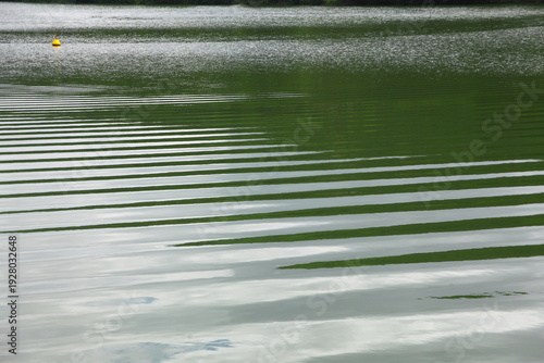 Calm Green Lake Water With Ripples, Horizontal Reflection Patterns and Small Yellow Buoy