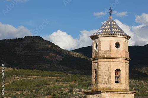 Historic Stone Bell Tower of Casas Altas in Valencia (Spain) With Tiled Roof Overlooking Mountain Landscape Under Blue Sky