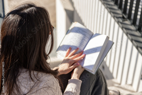 Photos Real woman sitting on outdoor steps in warm sunlight, relaxed and absorbed in reading a book, enjoying slow everyday life, real moments and simple quiet comfort