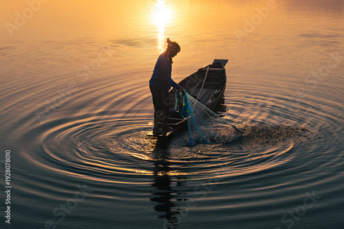 Quadro su tela Silhouette of fisherman throwing fishing net during sunrise at lake, Asian Thail