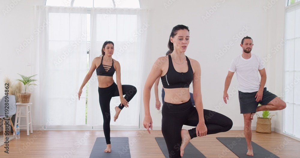 Obraz premium Professional yoga instructor is guiding a group through balance poses in a bright modern studio, focusing on physical wellbeing, mindfulness, and mastering skill.