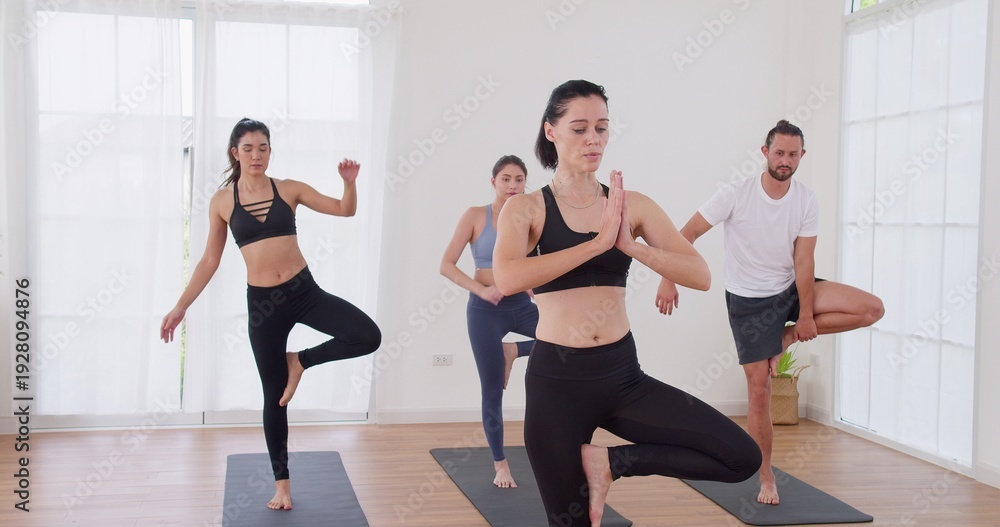 Obraz premium Professional yoga instructor is guiding adults on yoga mats in a modern studio, focusing on physical wellbeing, mental mindfulness, and mastering balance skills.