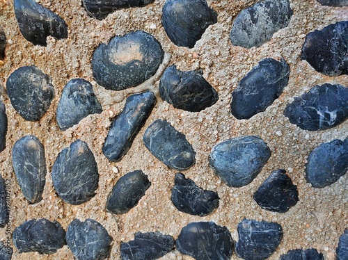 Dark round cobblestones embedded in a concrete base, showing the contrast of the decorative texture design on the playground floor