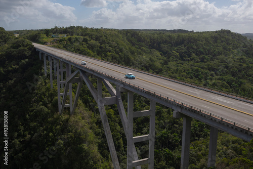 Aerial view of an old American classic car on empty high concrete bridge and highway road trough green tropical forest and mountains over a deep canyon. Bacunayagua Bridge, Matanzas, Cuba.