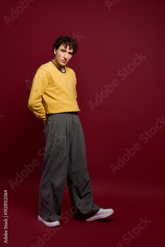 Fotografie Handsome man showcases stylish outfit against rich maroon backdrop with confiden