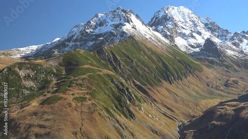 Panoramic view of cinematic fairytale snowy mountain peak and spectacular green valley in the Alps. Dreamlike alpine scenery glows in soft light shaping a magical serene landscape.