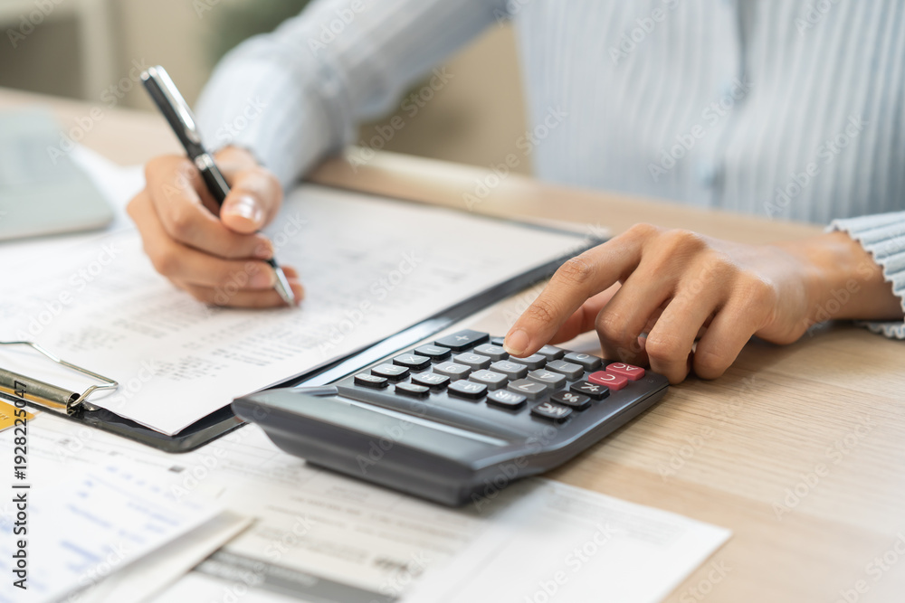 Fototapeta premium Stressed person asian young employee woman hand using calculator to calculate expenses of monthly and checking expenses from bill, receipt on table at home. Business and finance of banking concept