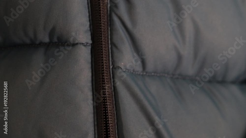 Opening a zipper on a dark puffer coat, close-up of fingers pulling down the slider.
