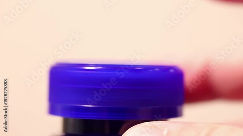 Macro close-up of a hand screwing on a blue plastic bottle cap.
