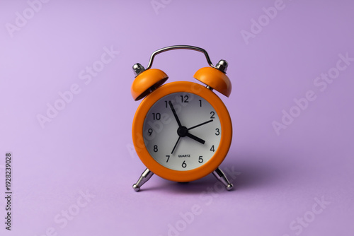 Fotografie Retro orange alarm clock with bells on a pastel purple background, studio shot