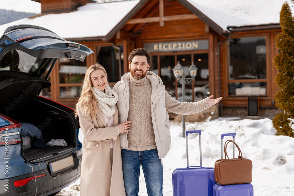 Fototapeta premium Smiling couple arriving at a ski resort hotel, reaching winter vacation destination