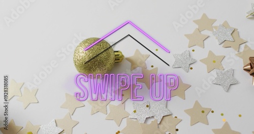 Displaying centered purple neon SWIPE UP text overlay glowing on light tabletop, with gold bauble