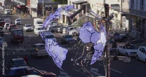 Framing wooden utility pole displaying digital globe over downtown street, with power lines, sedans