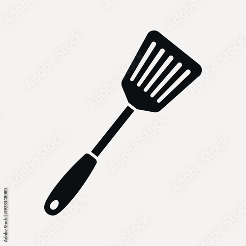 Black slotted spatula kitchen utensil with oval handle on a light beige background cooking tool