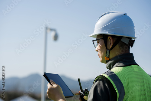 Schilderij op canvas Engineer wearing safety helmet holding tablet and walkie-talkie during on-site i