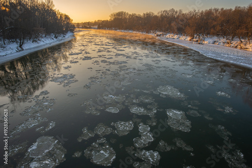 Soft morning light bathes the serene river, where chunks of ice drift lazily along the water's surface