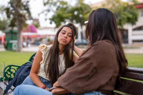 Young woman looking tired while friend comforts her on a park bench
